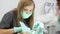 Female assistant, male dentist in face masks work in modern dental clinic. Nurse, stomatologist using dental instruments