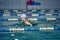 Female athlete in a green-black swimsuit is swimming in the style of breaststroke.