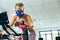 Female athlete with oxygen mask checking time while exercising with exercise bike in fitness studio