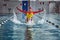 Female athlete in a red-yellow swimsuit makes a jump for joy in the pool.