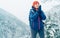 Female backpacker with backpack dressed warm down jacket warming palm hands and enjoying snowy mountains landscape while she