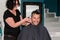 Female barber working with hair clipper, shaving young man\'s head