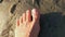 A female bare foot stands on wet sand and raises toes