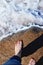 Female barefoot feet  stand on a granite stone on the coast with a sea wave and white foam