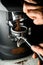 Female barista grinding coffee on professional grinder machine in coffee house closeup