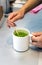 Female barista hand stirring matcha green tea on a mug.