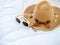 Female beach hat ornate with colorful ropes, boater straw hat flying and white trendy sunglasses on the white bed.