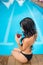 Female in black bikini sitting on the edge of swimming pool and drinking beverages on the background of perfect water