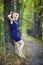 Female in blue dress leaning against a tree trunk in autumn linden tree alley