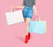 The female body part wore pink skirt jean and red boots. Carrying a shopping bag in many pastel colors on pink background