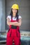 Female builder stands with arms crossed on a construction site dressed in work overalls and a yellow hard hat