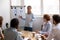 Female business coach standing near whiteboard talking to diverse team