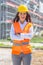 Female businesswoman wearing jeans, safety vest and helmet stands confidently in front of the construction covered in scaffolding