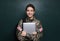 Female cadet with backpack and laptop near chalkboard. Military education