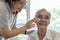 Female caregiver assisting to apply sunscreen lotion on the face of senior woman,granddaughter using skin care cream for elderly