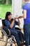 Female caregiver giving cup of tea to woman on wheelchair