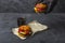 Female chef in black gloves putting freshly prepared grilled beef burger on parchment paper on a dark table. American snack