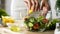 Female chef hands squeezing fresh lemon juice into bowl with salad, vitamins