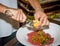 Female chef preparing steak tartar in kitchen with a special sauce and lemon