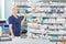 Female Chemist Standing By Shelves In Pharmacy