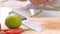 Female chief cutting tomato into pieces with knife on wooden chopping board.