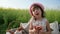 Female child in panama with bun on nature, Weekend at picnic, Girl on flower meadow with pastries and milk, Happy joyful