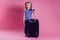 Female child striped blue white t-shirt sitting on a large travel suitcase dream flies rest on the sea shore pink