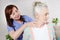 Female chiropractor looking at senior woman with neck pain in the medical office or bedroom. Therapy rehabilitation of the elderly