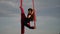 Female circus artist showing her flexibility and splits with red aerial silk on the sky background is slow motion