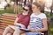 Female classmates sit closely to each other, read information from one book while sit on wooden bench, have focused expressions, d