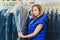 Female cleaner in laundry shop or textile dry-cleaning next to clean clothes in garment bags.