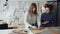 Female clothing designer is drawing outlines of new garment on fabric with chalk while her colleague is helping her and