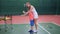 Female coach dressed in short white sport dress is teaching little boy to play at indoor court. Professional tennis