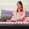 A female composer in pajamas and a cat writes sheet music on paper. Writing music at home with a digital piano