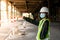 Female construction engineer Asians wearing safety hats and green vests stand to watch work and point fingers at a construction si