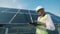 Female constructor is walking along a solar panel with a computer