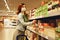 Female consumer purchasing goods at mall, walking among shelves. Girl with mask shopping of food