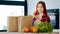 Female consumer woman caucasian buyer unpacks groceries from paper eco-packaging bag stands in modern kitchen. Cute