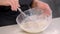 A female cook pastry chef whips dough in a glass bowl with a metal whisk.