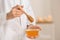 Female cosmetologist holding dipper and bowl with honey on blurred background