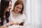 Female Couple using smart phone shopping online and researching online on tablet while sitting on sofa