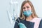 Female dentist in blue gloves holding in hand a mouth mirror and periodontal explorer scaler, blurred background of clinic with