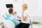 Female dentist holding a mirror for a male client of a dentistry who is smiling checking his teeth.