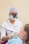 Female dentist in mask with loupe binoculars examing and curing teeth of patient