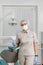 Female dentist in a medical mask and cap standing in a dental clinic among modern dental equipment. Portrait of a female