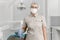 Female dentist in a medical mask and cap standing in a dental clinic among modern dental equipment. Portrait of a female