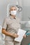 Female dentist in a medical mask and cap standing in a dental clinic among modern dental equipment. Portrait of a female