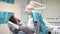 Female dentist sits down next to patient preparing dental lamp to examining.