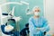 A female dentist wearing a medical mask and rubber gloves poses for the camera and folds her arms in her office