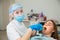 Female dentist work with light-curing seal, patient with caries on chair.